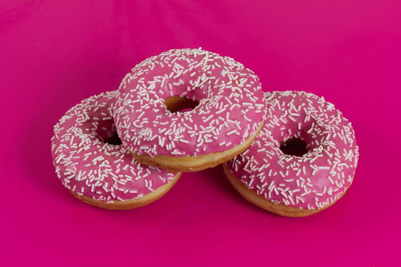 3 donuts rosas sobre un fondo fucsia